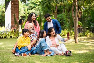 Fototapeta premium Happy Indian family taking selfie together outdoors, three generations bonding in park