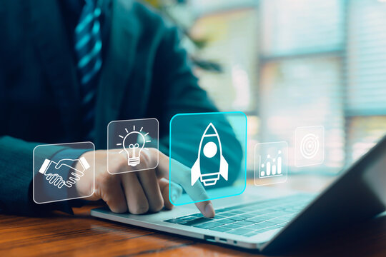 Business person tapping a digital startup rocket icon on a laptop with innovation, ideas, growth analytics, and goal symbols, representing entrepreneurship, business development, and modern technology