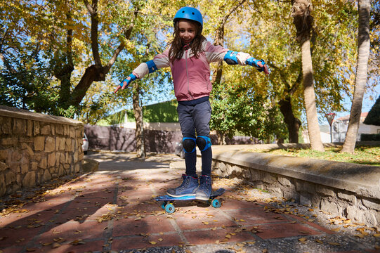 Young Girl Roller Skating Outdoors in Autumn Park with Helmet and Knee Pads