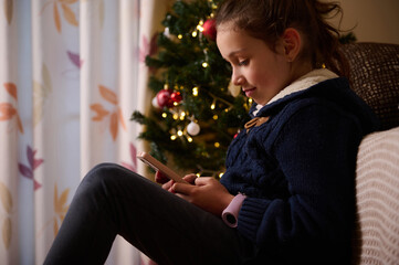 Girl Relaxing By Christmas Tree Using Smartphone In Cozy Living Room