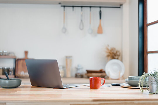 Red coffee mug on wooden table with laptop and kitchenware in bright modern kitchen, cozy morning scene