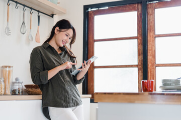 Young woman using tablet in bright kitchen smiling with relaxed mood