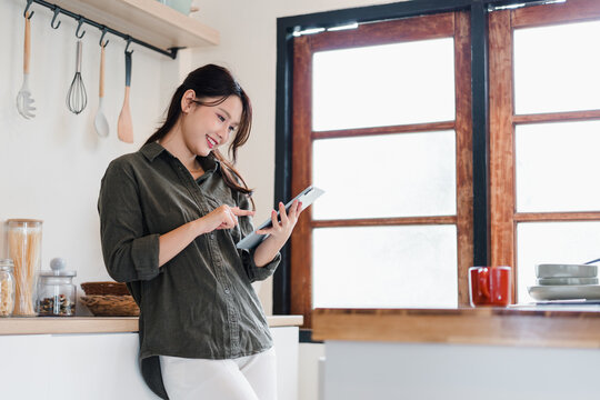Young woman using tablet in bright kitchen smiling with relaxed mood