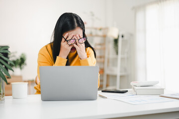 Woman rubbing eyes while working on laptop, tired and stressed at home desk
