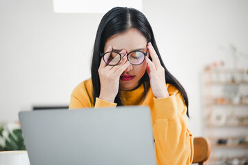 Young woman with headache rubbing eyes while working at laptop, tired and frustrated