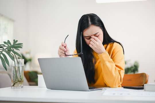 Woman with headache rubbing eyes while working on laptop at home in casual sweater - Powered by Adobe
