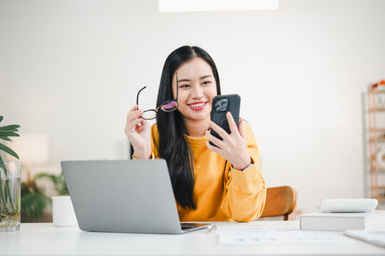 Young woman smiling while checking smartphone at home workspace, cheerful