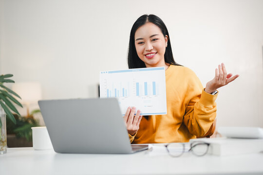 Young woman in yellow sweater presenting sales chart during video meeting, smiling and confident