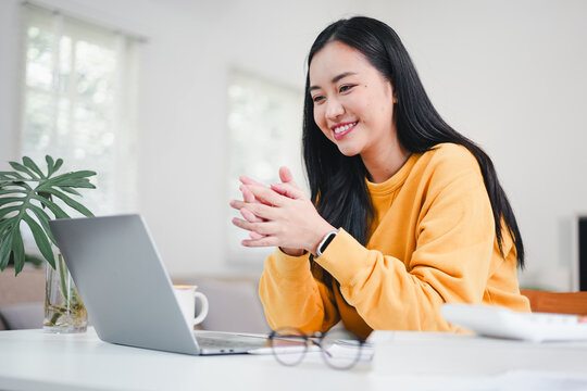 Young woman smiling during video call at home in casual yellow sweater, relaxed and engaged