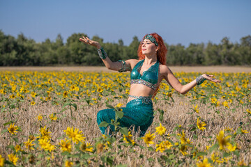 A red-haired oriental dancer poses in a field of sunflowers.
