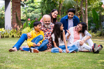 Indian family of three generations smiling and bonding outdoors on green park lawns