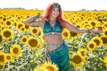 A red-haired oriental dancer poses in a field of sunflowers.