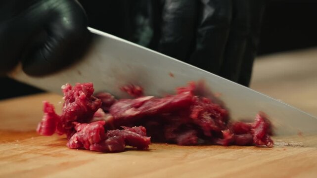 Working with beef, cut steak Chef cooking Raw beef meat tartar with sauce, man cutting steak tartare, making delicious french dish in modern restaurant. Fresh eco angus meat. 
