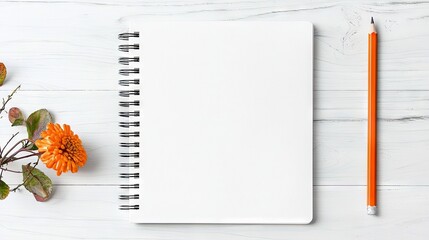 An open spiral-bound notebook with blank pages, an orange flower with leaves, and an orange pencil are arranged on a white wooden table. The scene is lit with s