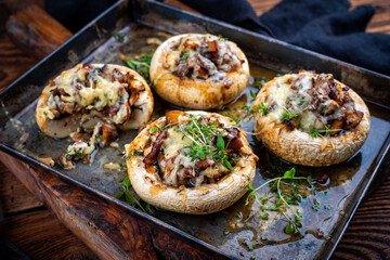 Portabello mushrooms stuffed with cheese and fresh herbs, oven baked with raclette cheese served as close-up on a backing sheet