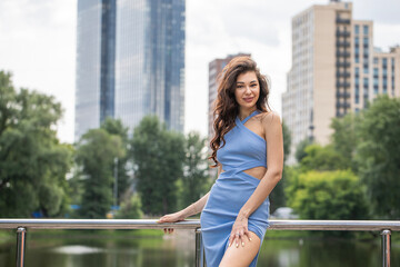 Fototapeta premium Young beautiful brunette woman in blue knitted dress posing in summer park