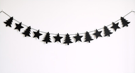 Black Christmas garland with stars and trees hanging on a white wall. Minimalist paper bunting decoration for holiday season. Gothic Gothmas style background