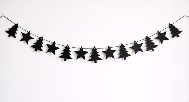 Black Christmas garland with stars and trees hanging on a white wall. Minimalist paper bunting decoration for holiday season. Gothic Gothmas style background - Powered by Adobe