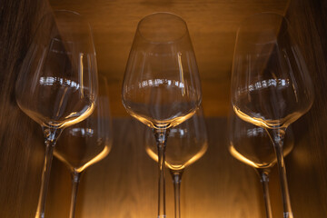 Row of empty wine glasses arranged on a wooden shelf with warm golden lighting in a stylish restaurant or bar interior.