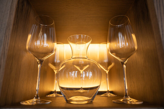 Wine glasses and a glass decanter displayed symmetrically on a wooden shelf with golden ambient backlight in an upscale dining venue.