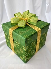 Beautifully wrapped green gift box with decorative ribbon and bow on white fabric