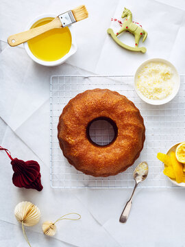 Overhead shot displays a golden lemon bundt cake on a wire rack, along with ingredients like lemon zest and a buttery glaze. Festive decorations add a holiday touch