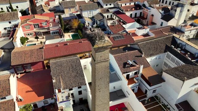 Drone aerial above Puente Genil Andalusia Spain showing white storks nesting on a tall old brick chimney above whitewashed roofs and historic town architecture