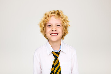Bright smile of a cheerful schoolboy in uniform with a stylish striped tie