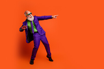 Elderly man in bright purple suit points playfully against orange background in a retro disco inspired lifestyle photo