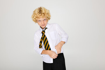 Blonde boy in wavy hair adjusts his striped tie while posing in studio