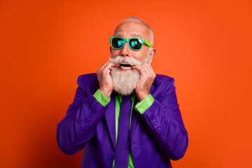 Vibrant retro bearded man in purple suit wearing green sunglasses smiles against bright orange backdrop