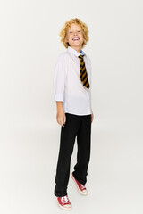 Blonde boy in school uniform poses confidently in studio setting with striped tie © Bliss
