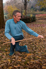 Senior man performing tai chi moves with a wooden staff in a park environment