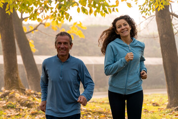 Happy mature couple jogging together in a park during autumn