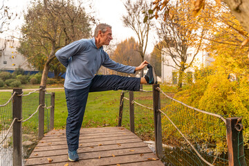 Senior man stretching on a park bridge for health and fitness during autumn