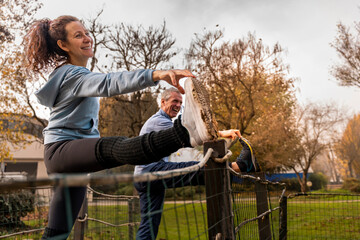 Senior couple enjoying leg stretches with smiling faces in an autumn park