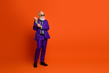 Fototapeta premium Modern retro styled elderly man in purple suit and green tie posing against bright orange background
