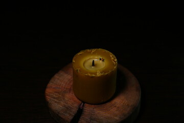 Closeup nature beeswax candle not igniting yet on a wood on dark black background in a center with...
