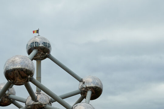 Detailed view of the Atomium's upper dome structure topped with the Belgian flag. The overcast sky enhances the reflective metallic spheres of this iconic Brussels landmark.