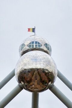 The top sphere of the Atomium in Brussels flies the Belgian flag. A detailed architectural capture highlighting national pride and futuristic design elements under an overcast sky.