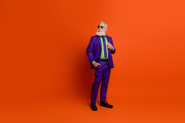 Stylish elderly man in a purple suit with neon green shirt posing confidently on a bright orange background