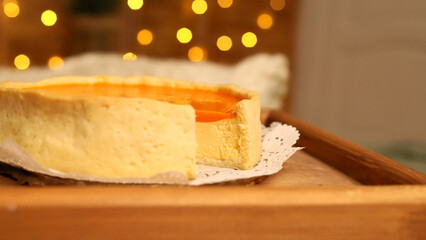 A homemade cheesecake sits on a wooden tray, partially sliced, with a warm, festive atmosphere highlighted by soft glowing lights. Perfect for New Year and Christmas celebrations