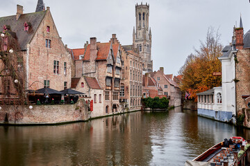 Picturesque view of a canal in Bruges, Belgium, featuring historic Flemish architecture and the iconic Belfry of Bruges in the background. Autumn colors and still waters create a peaceful atmosphere 