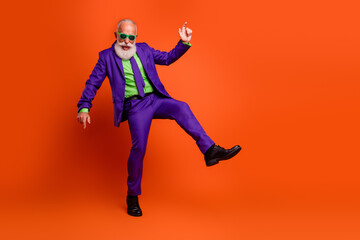 Elderly bearded man dancing in a bright purple suit with green shirt against an orange background at a festive party