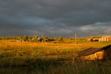 Golden rural landscape on Solovetsky Island with wooden houses, fields and dramatic storm clouds at sunset.