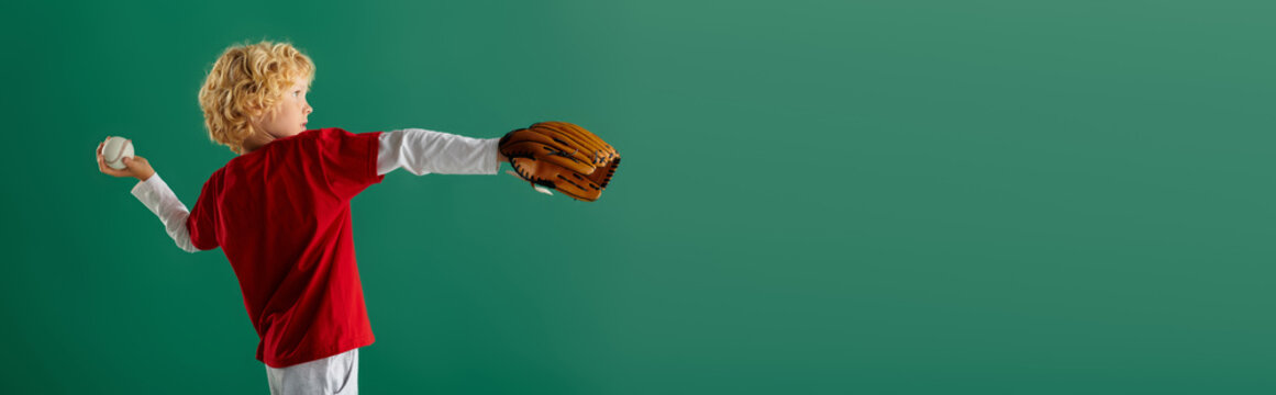 Blonde boy in red clothes gets ready to play baseball in a bright studio setting