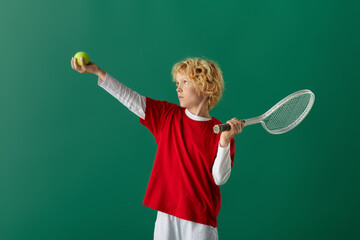 Blonde boy prepares to serve a tennis ball on a vibrant green background