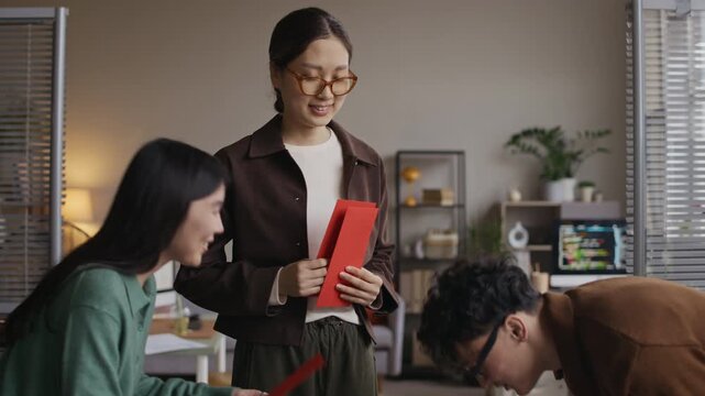 Medium shot of cheerful Asian employees exchanging red envelopes while celebrating Tet in modern office