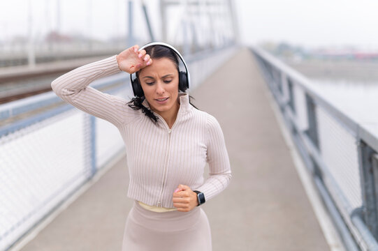 Woman running on bridge wiping sweat from forehead - Powered by Adobe