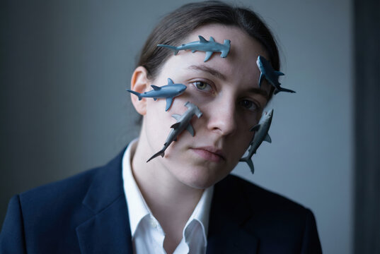 Introspective Young Professional with Shark Toys Affixed to Face in a Bold Contrast of Dark Suit and Soft Background